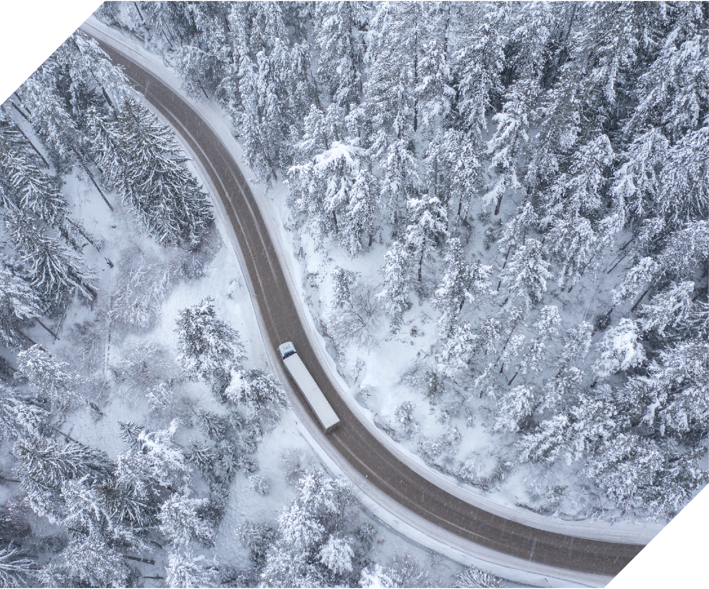 birds eye view of a semitruck driving through snowy forest roads