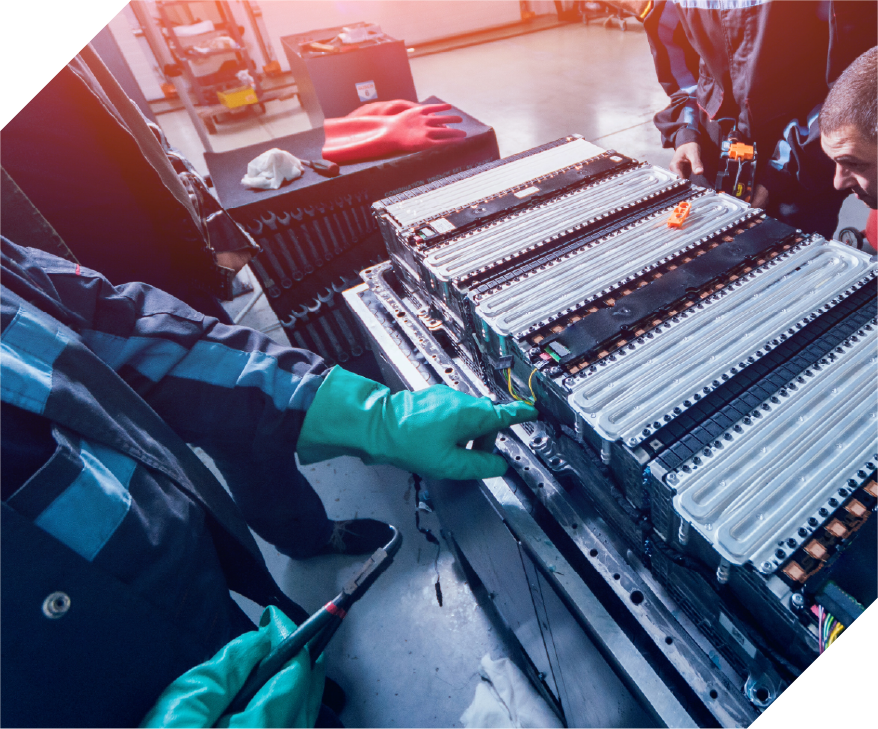 three people working on a large battery cell, one wears green rubber gloves and points to a section