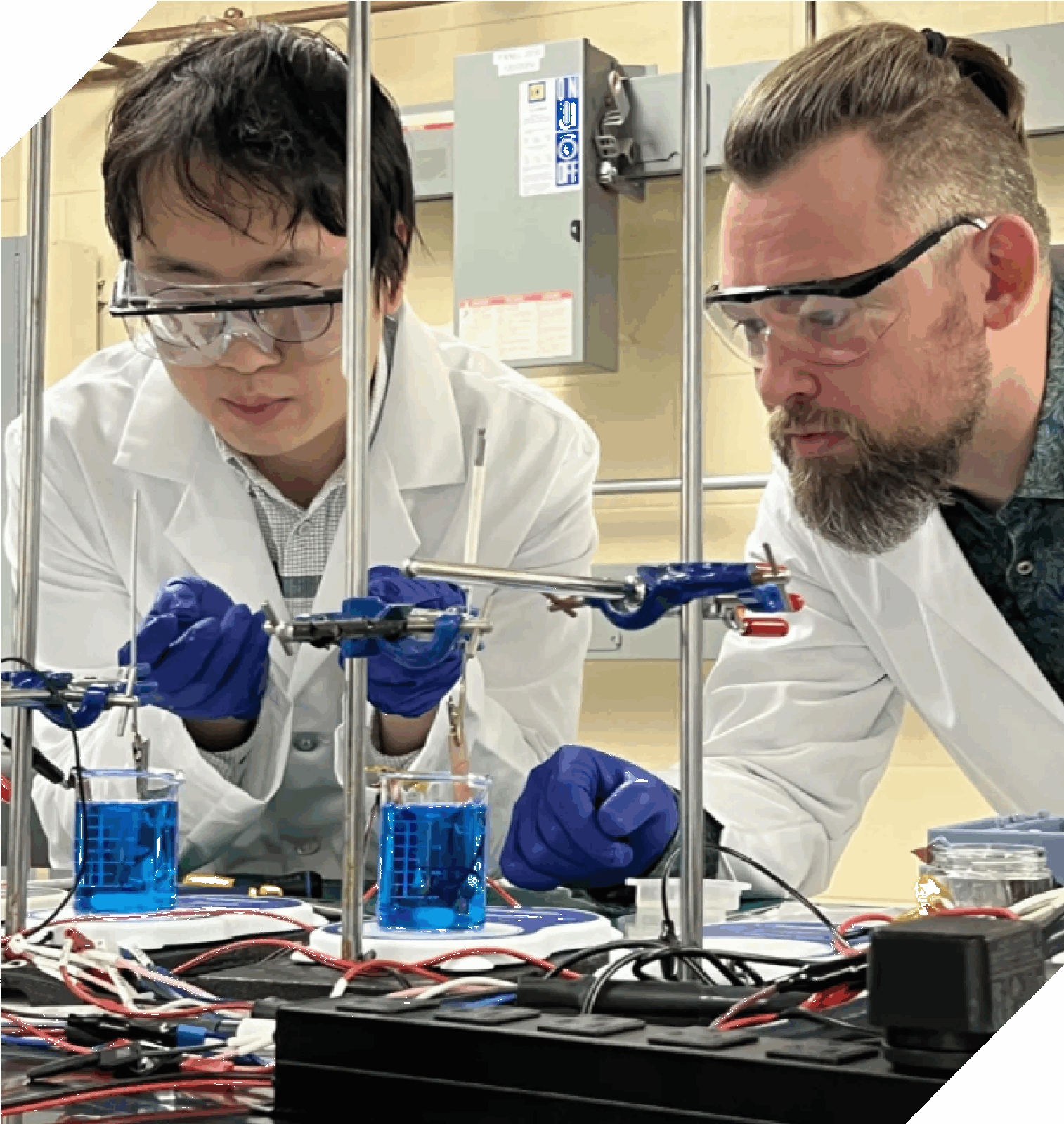 two scientists wear safety glasses and gloves while working with electrical equpiment